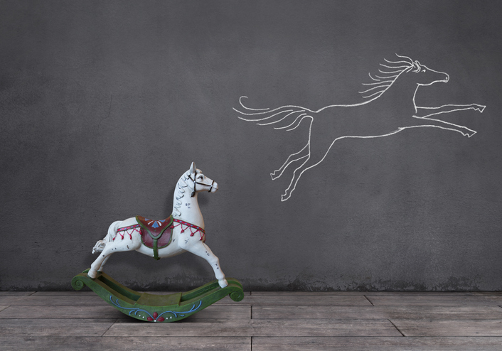 Ein Schaukelpferd vor einer Tafel mit einem gezeichnetem Pferd darauf.